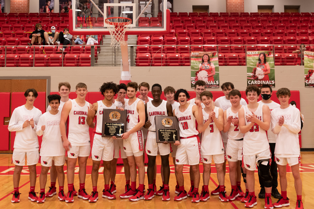 Farmington Varsity Boys Basketball team in uniform standing on the Cardinal Arena court holding their Championship trophies