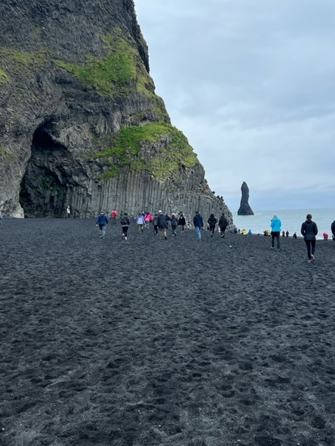 students walking toward a cave on a black sand beach