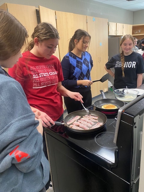 students standing over a stove cooking eggs