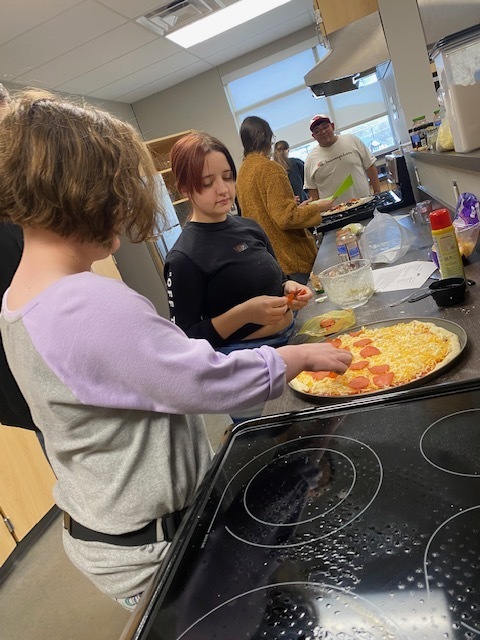 students standing over a stove making pizza