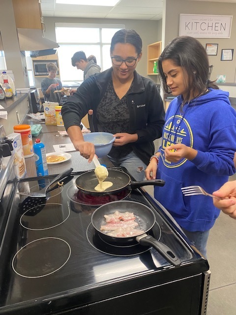 students standing over a stove making pancakes 
