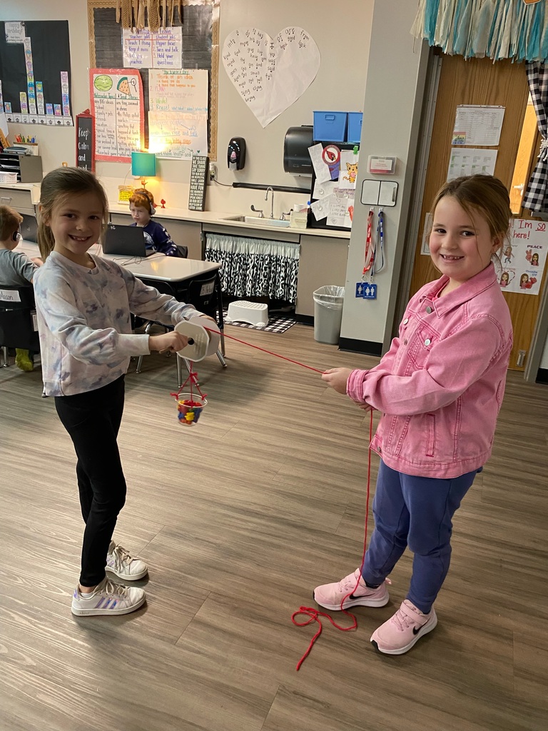 Students smiling and holding a pulley they created in the classroom
