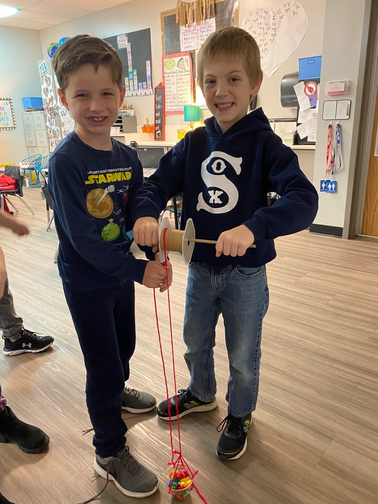 Students smiling and holding a pulley they created in the classroom