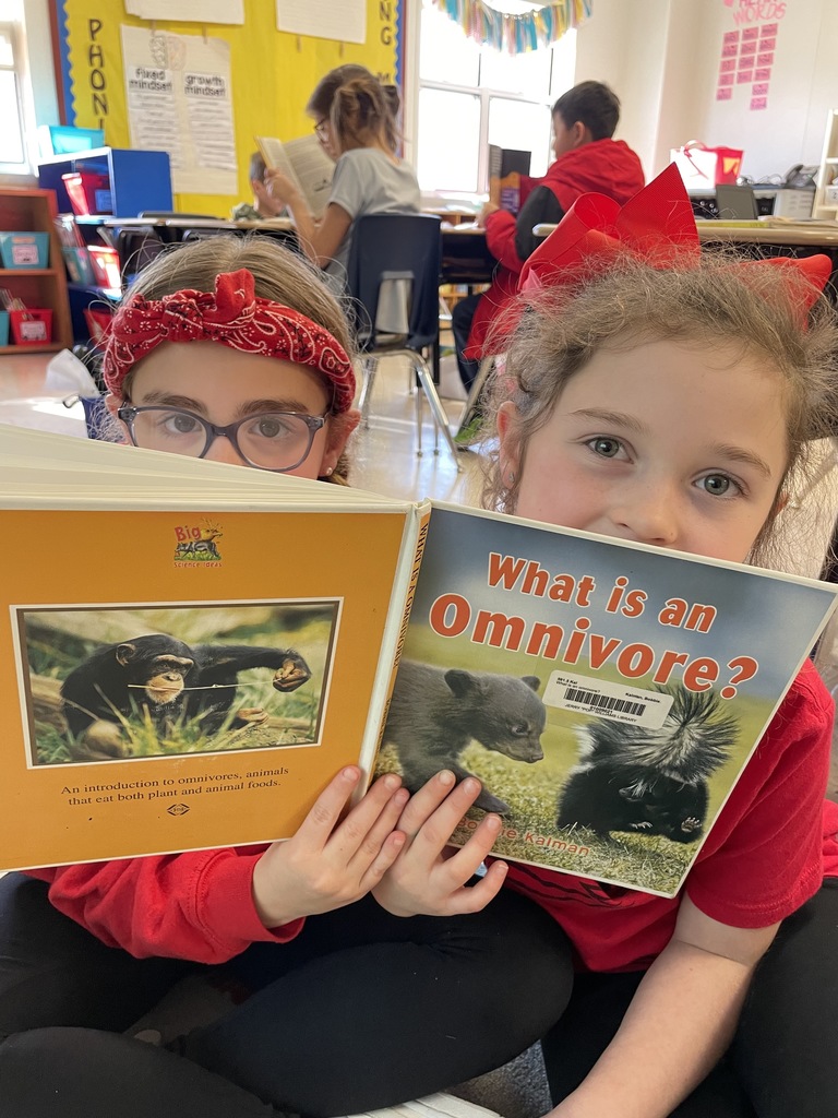 Two students holding a book up where you can only see their eyes.
