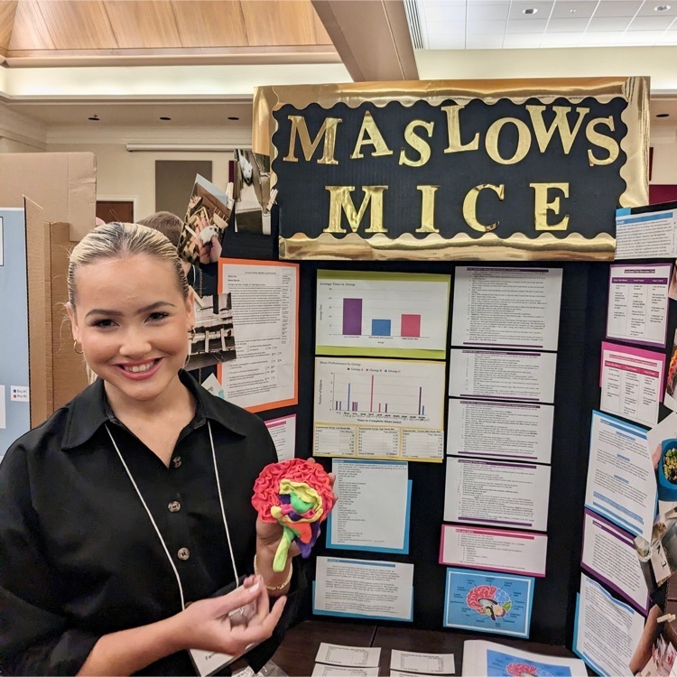 student posing in front of science fair board 