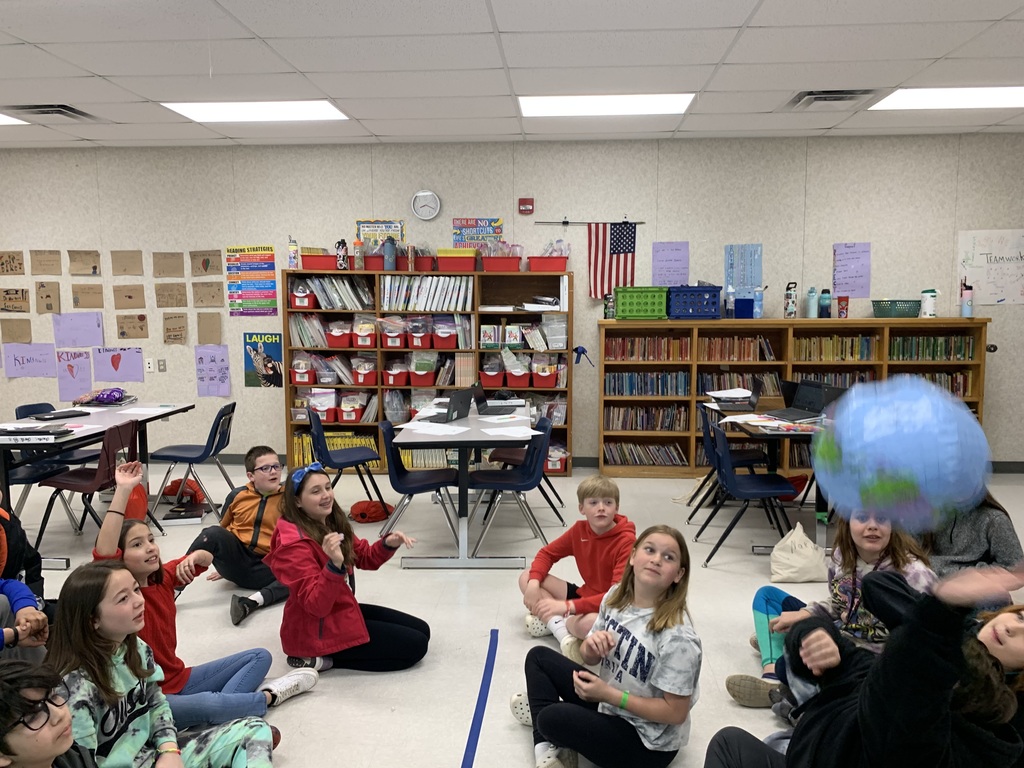 6th Grade Celebration! Students are sitting in the floor of the classroom playing a game with a blow up world ball.