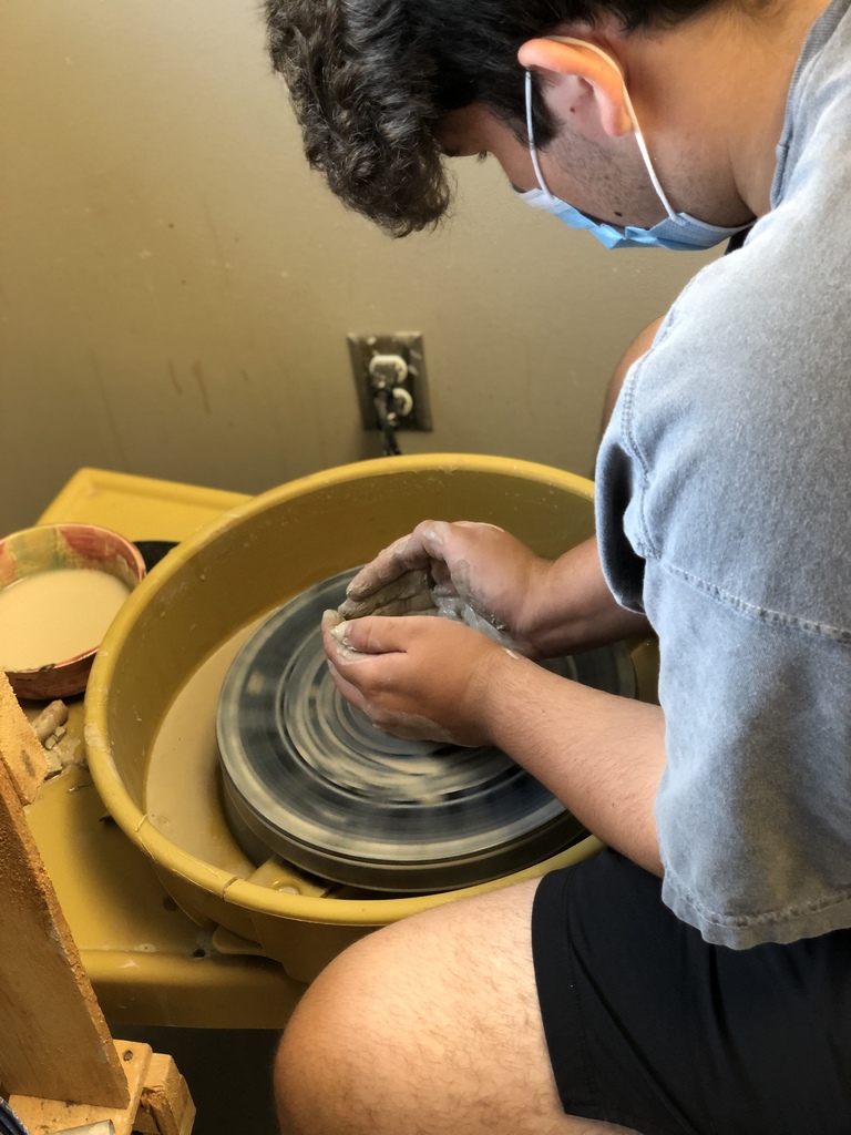 Student molding clay on a pottery wheel